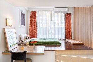 A hotel room with a bed, a desk with a chair, a vase with flowers, a framed picture, and a window with curtains. - P2 Boutique Hotel (Bangkok)