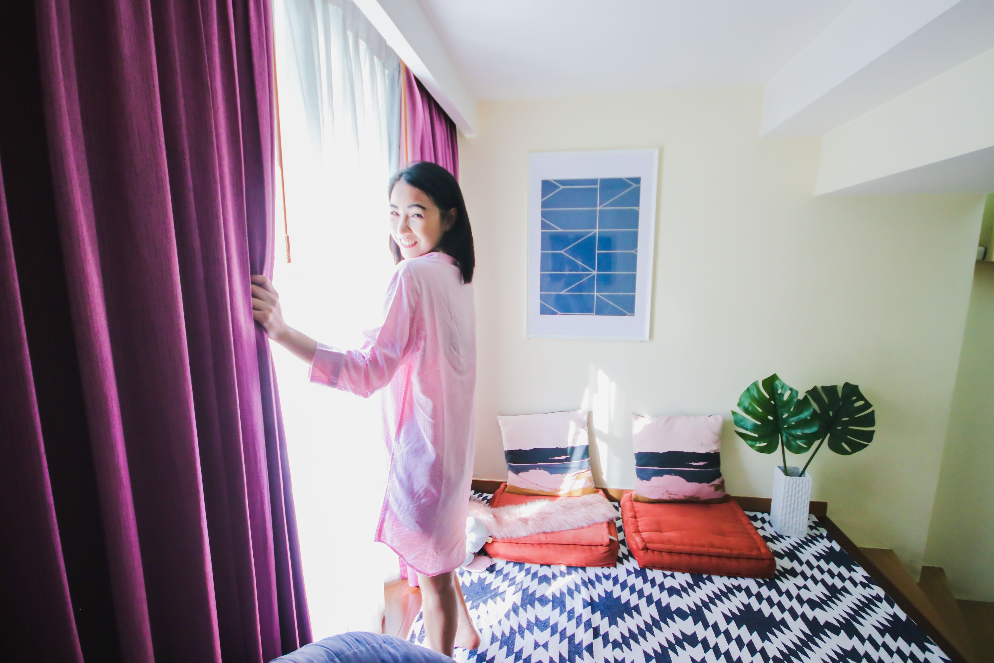 Una habitación con cama, ventana con cortinas, un cuadro en la pared y una planta en maceta.