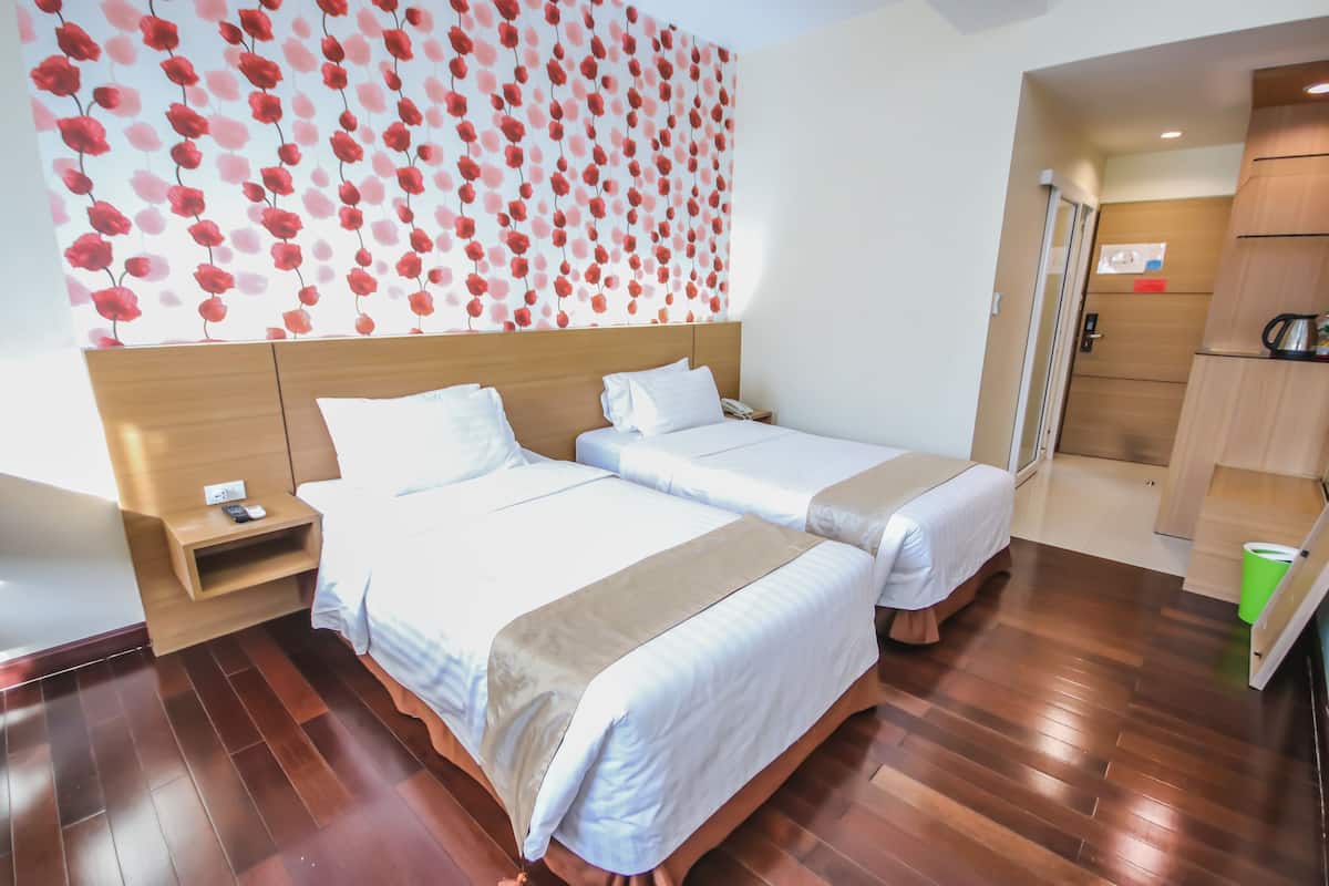 Hotellihuone, jossa on kaksi sänkyä, puinen pääty, yöpöytä, punavalkoiskuvioinen seinä ja puulattia.