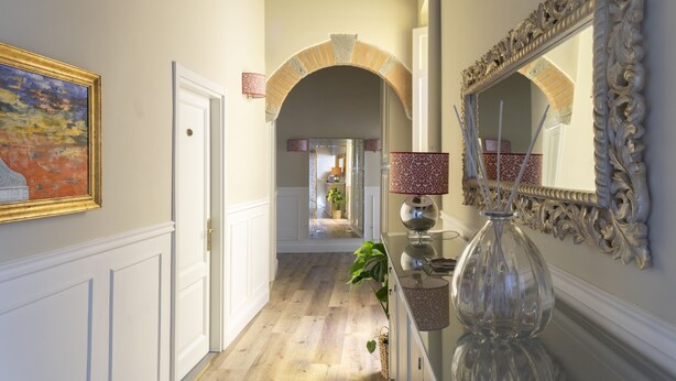 A hallway with a mirror, a vase, and a painting on the wall. - Residenza Della Signoria (Florence)