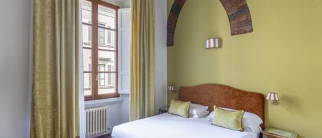 A bedroom with a large bed, a nightstand, a window with curtains, and a radiator.