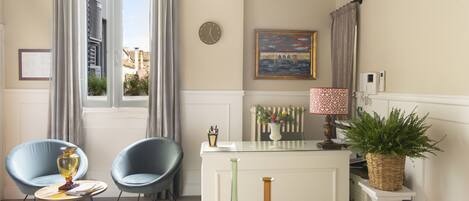 A room with a dining table, two chairs, a small round table with a vase, a clock on the wall, a painting, and a potted plant.