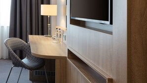 Une chambre d’hôtel avec un bureau en bois, une chaise, un téléviseur fixé au mur et une lampe.