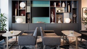 Un salon moderne avec deux fauteuils gris, une table basse et un téléviseur fixé au mur, au-dessus duquel se trouvent des étagères décoratives.