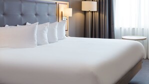 A neatly made bed with white linens and a tufted headboard, a bedside lamp, and a round table beside the bed. - Leonardo Hotel London Watford (Watford)