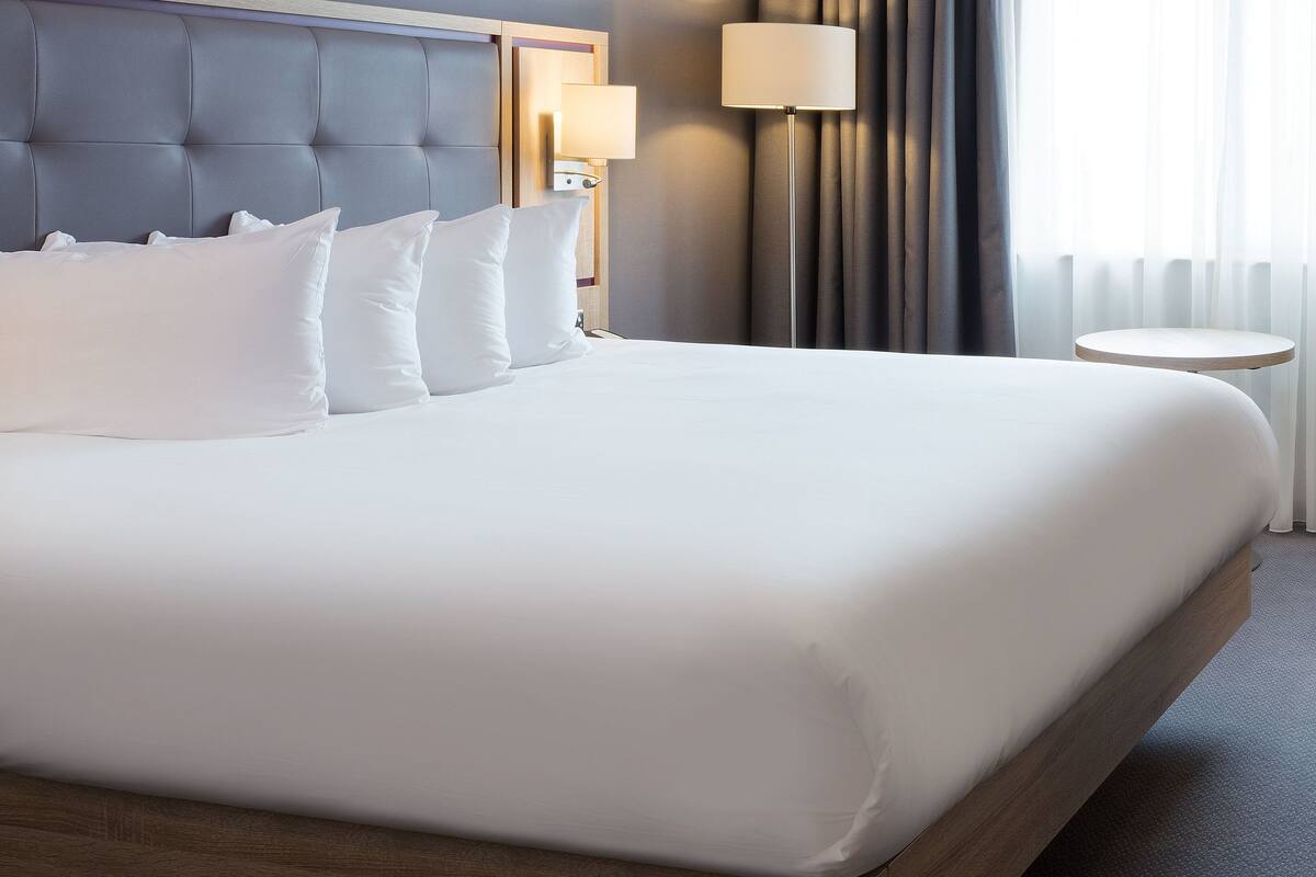 A neatly made bed with white linens and a tufted headboard, a bedside lamp, and a round table beside the bed.