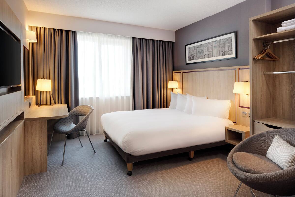 Een hotelkamer met een bed, bureau, stoel, televisie en garderobe.