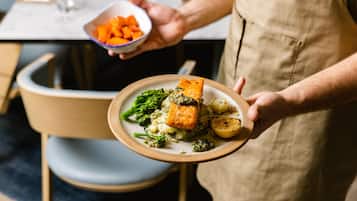 Una persona sosteniendo un plato de salmón, brócoli y patatas.