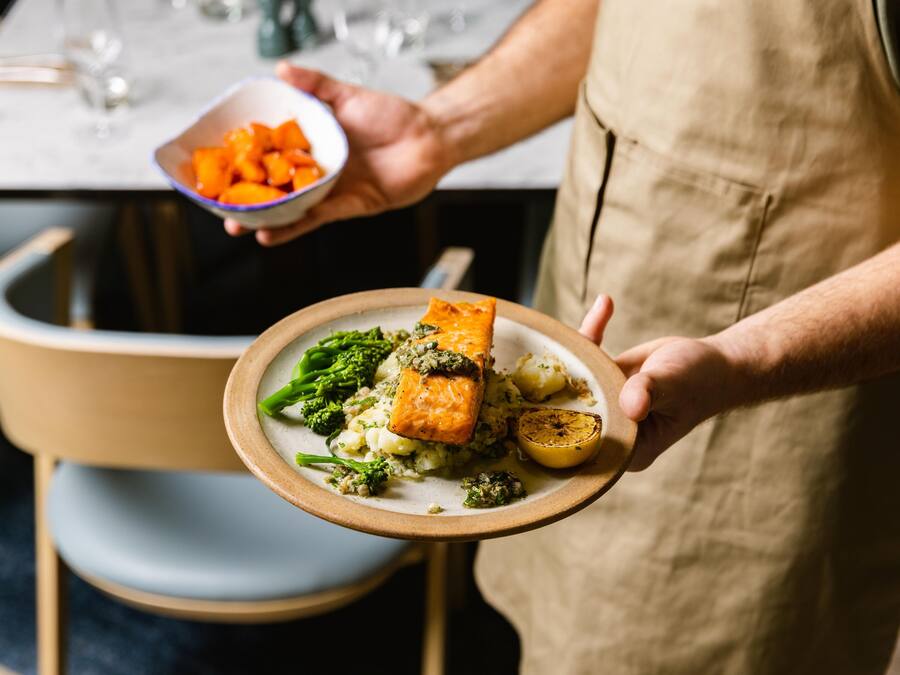 A person holding a plate with salmon, broccoli, and potatoes.