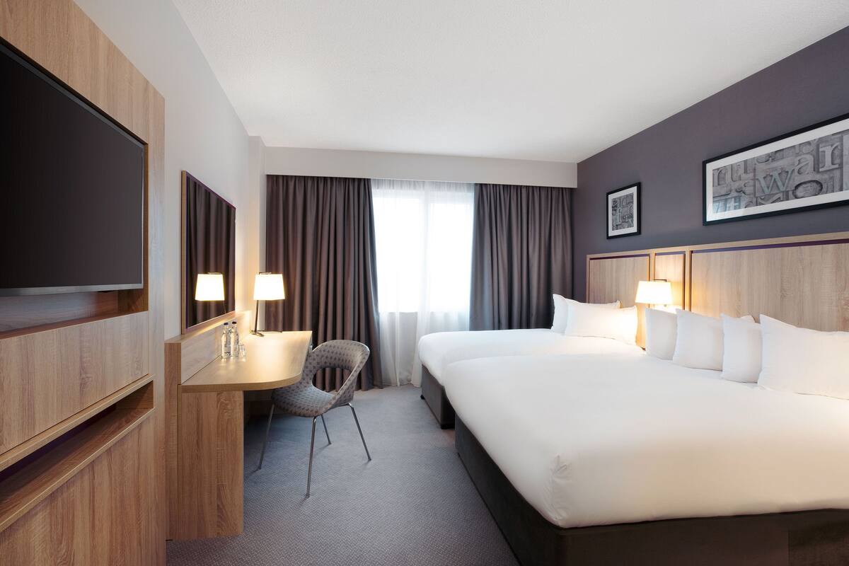 A hotel room with a bed, a desk with a chair, a television, and a window with curtains.