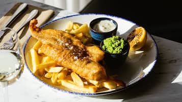 A plate of fish and chips with lemon wedges and a small bowl of tartar sauce, accompanied by a glass of white wine.