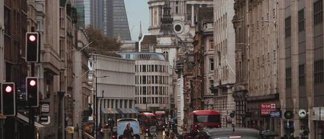 A busy urban street with historic buildings, a prominent dome structure, and modern skyscrapers in the background.