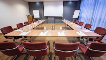 Kokoushuone, jossa on pitkä pöytä, punaiset tuolit, vesipulloja ja projektorikangas.