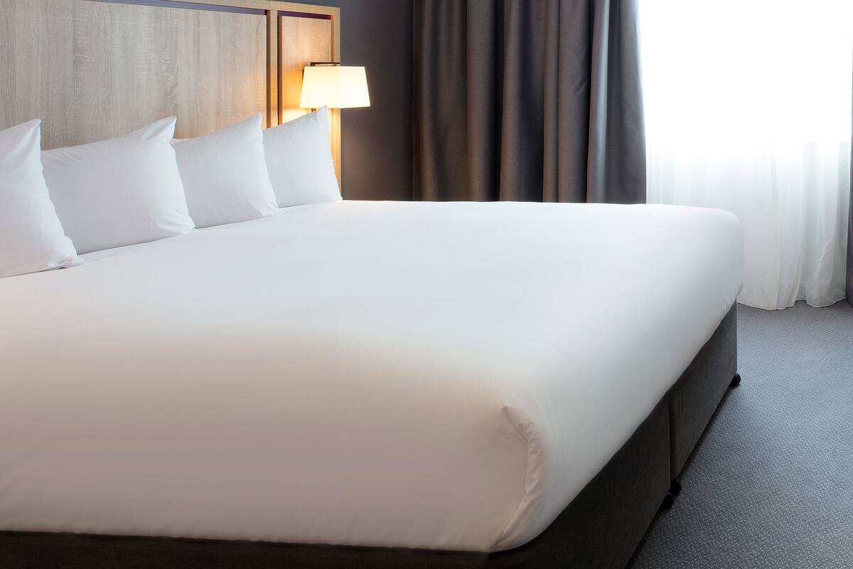 A large bed with white linens, a wooden headboard, and a bedside lamp.