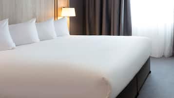 Una cama grande con sábanas blancas, un cabecero de madera y una lámpara de noche.