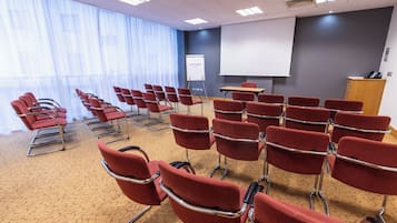 A conference room with rows of red chairs, a projector screen, and a whiteboard labeled "LEONARDO".