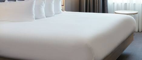 A neatly made bed with white linens, a tufted headboard, and a round bedside table.