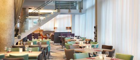 A modern restaurant with multiple dining areas, a staircase, and large windows.