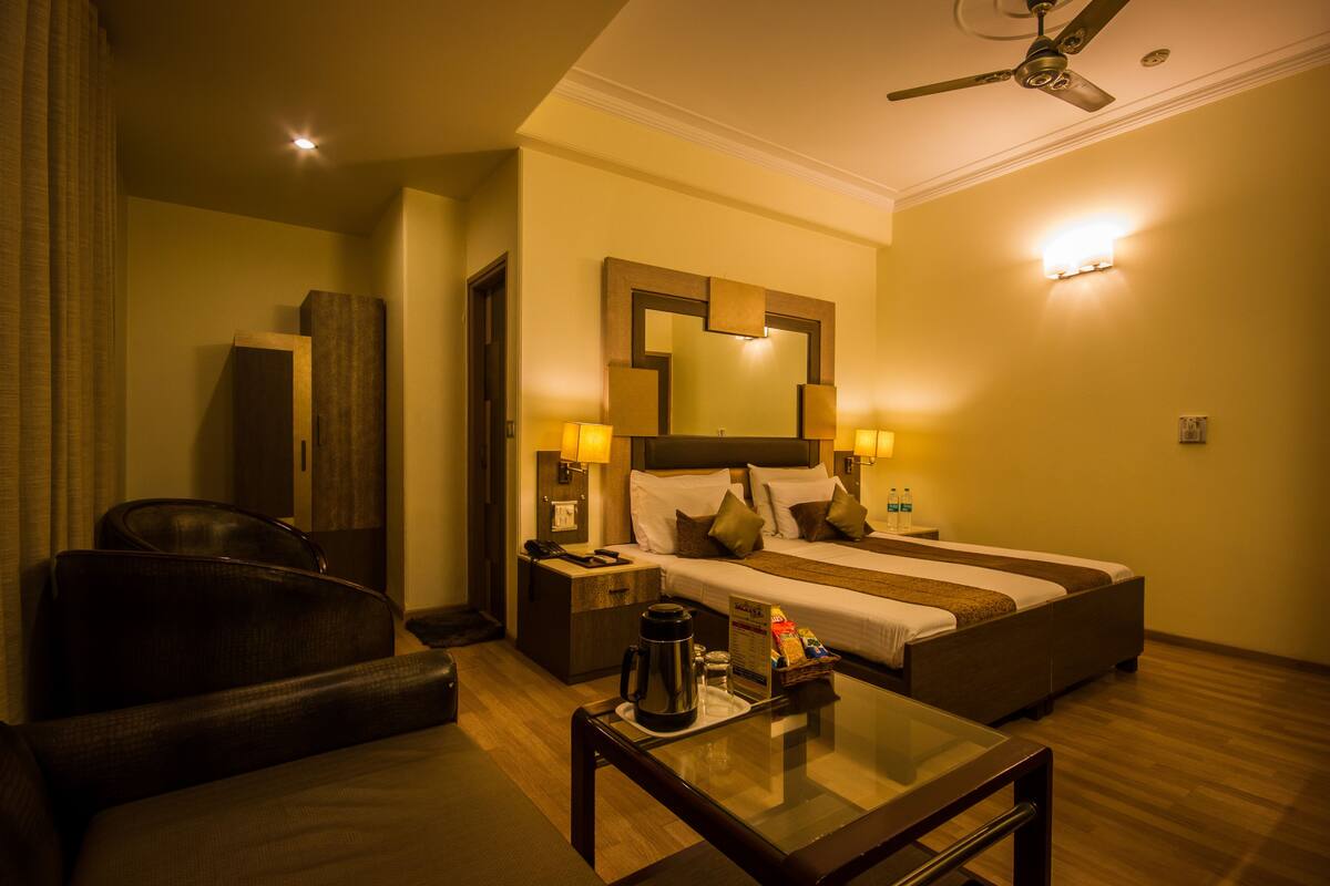 A hotel room with a bed, a desk, a chair, a coffee maker, and a mirror.