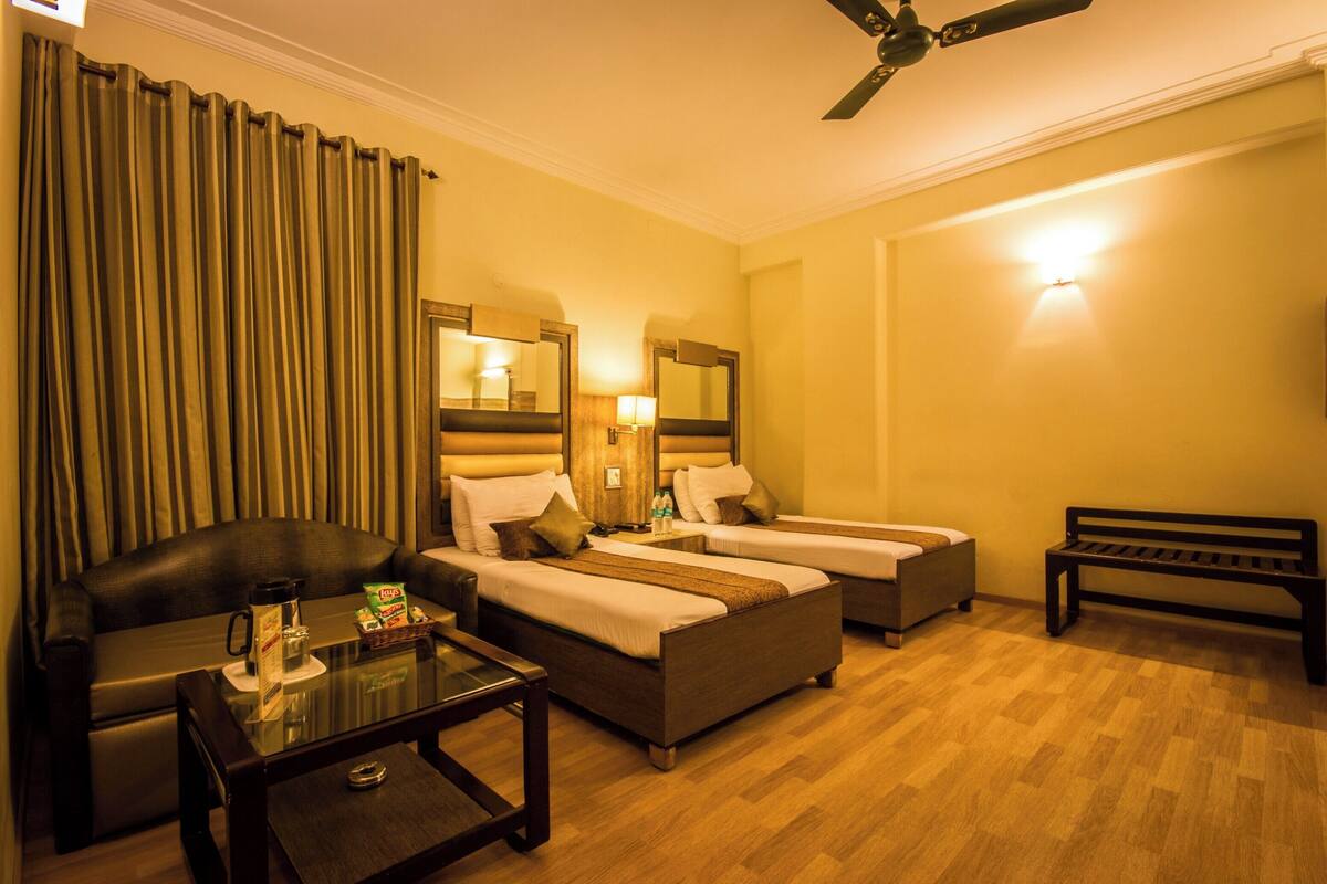 A hotel room with two single beds, a sofa, a coffee table, a bench, and a ceiling fan.