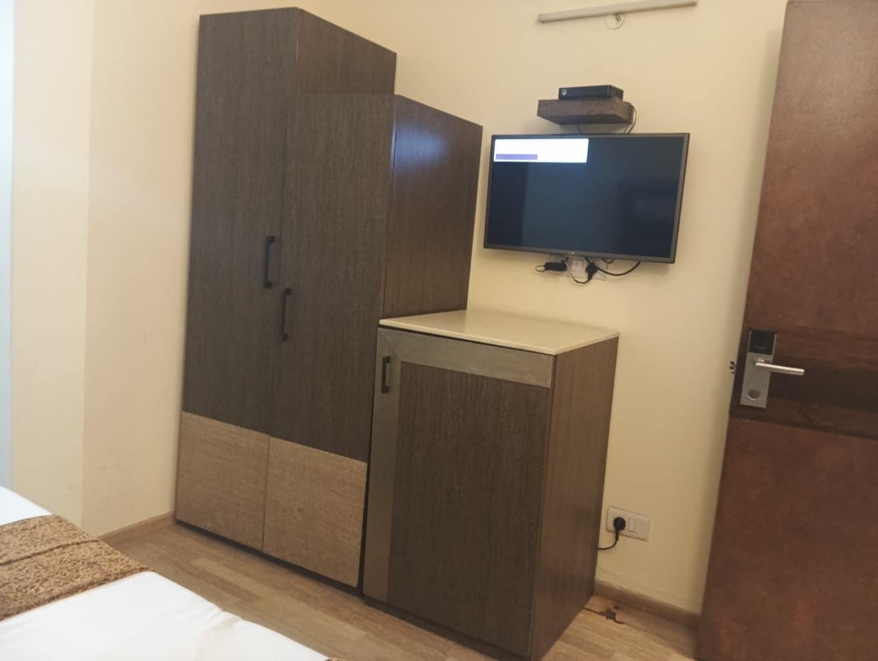 A bedroom with a wardrobe, a television mounted on the wall, and a door.