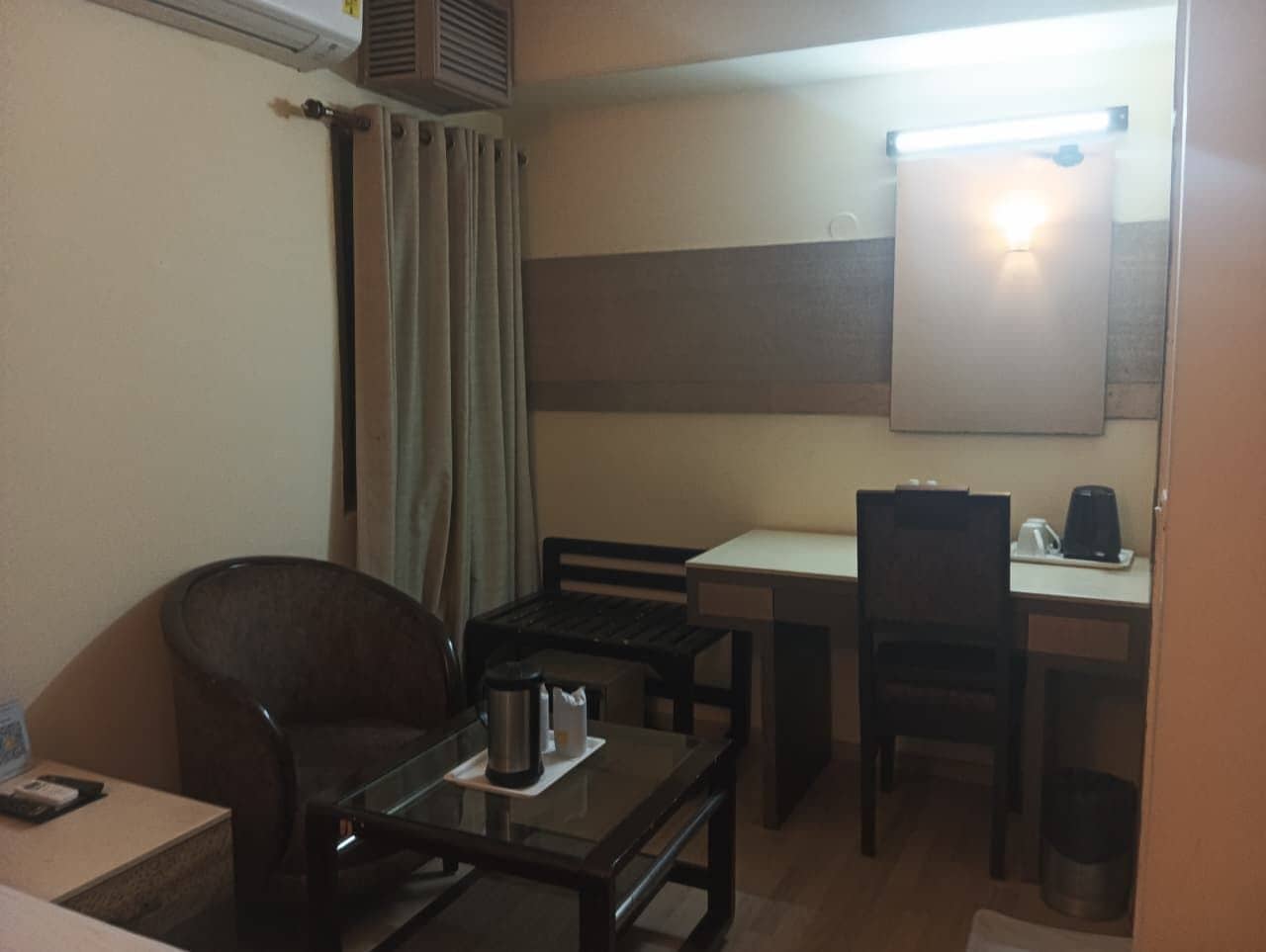 A compact hotel room with a single bed, a small table with a chair, a desk with a chair, and a mirror on the wall.