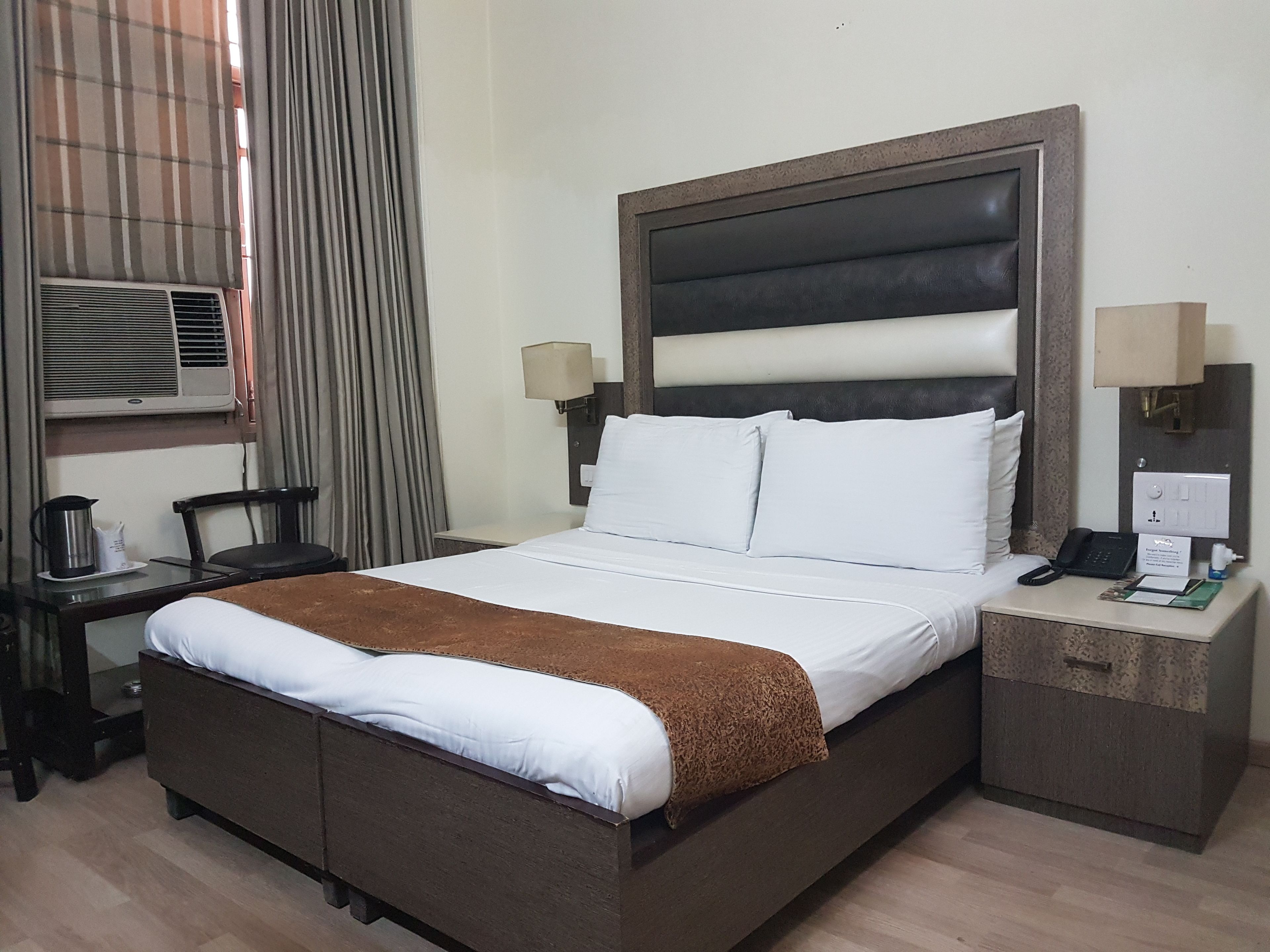 A hotel room with a bed, bedside tables, a lamp, a telephone, and an air conditioning unit.