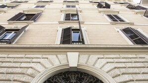 A building facade with multiple windows, some with shutters, and a decorative archway at the bottom.
