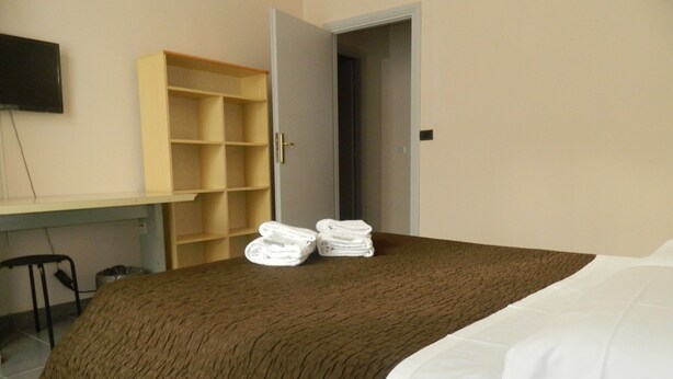 A hotel room with a bed, a TV mounted on the wall, a desk with a chair, and a wardrobe.
