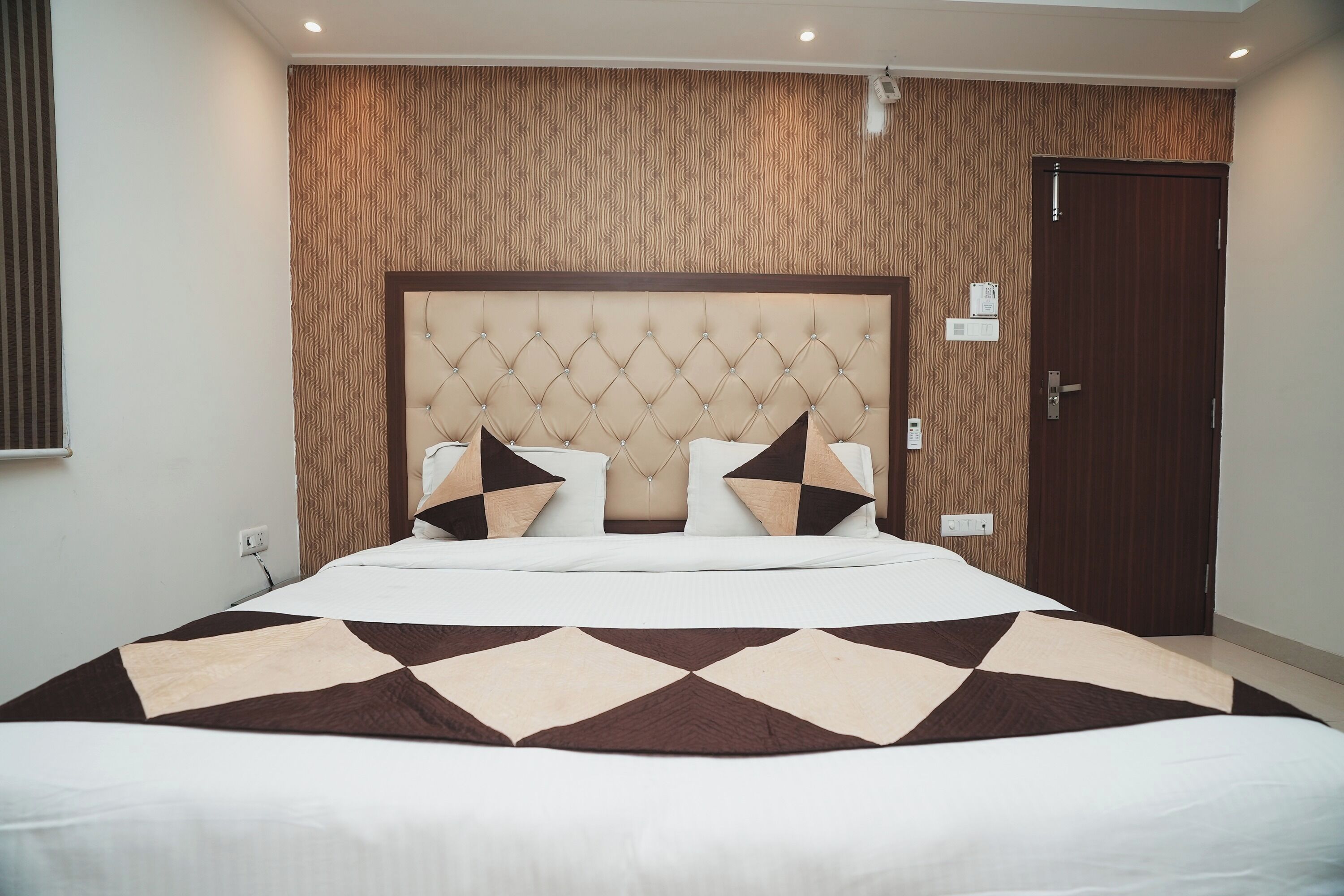 A hotel room with a large bed, a tufted headboard, and a patterned wall.