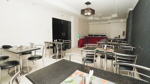 Un'area pranzo con diversi tavoli e sedie, una porta nera e una tenda rossa sullo sfondo.