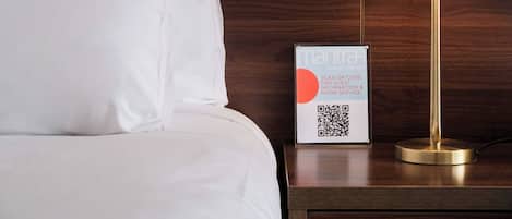 Habitación de hotel con cama, mesita de noche, lámpara y un cartel con código QR para servicio a la habitación.