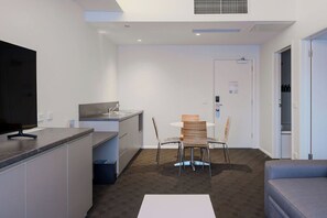 Une cuisine moderne dotée d’une cuisinière intégrée, un coin repas avec une table et des chaises, et un canapé gris.