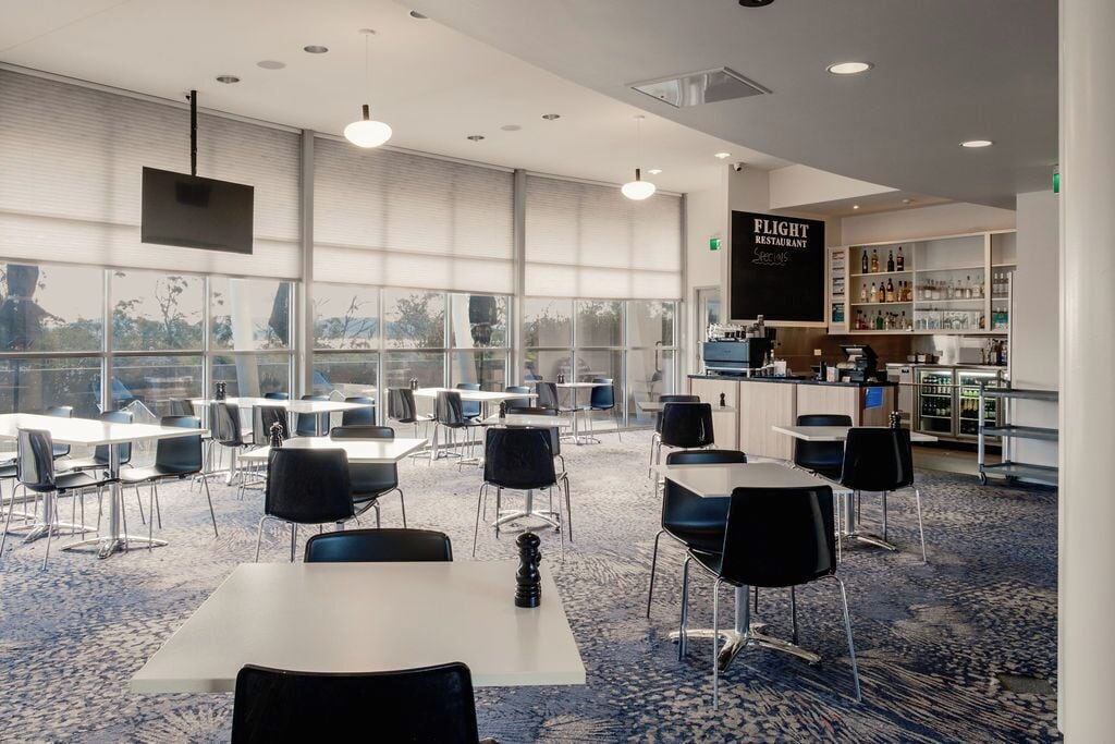 A modern restaurant with a bar area, large windows, and a carpeted floor.