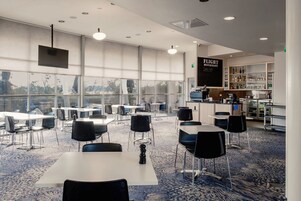 A modern restaurant with a bar area, large windows, and a carpeted floor.