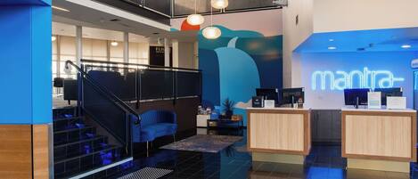 A modern hotel lobby with a reception desk, a staircase, and a mural.