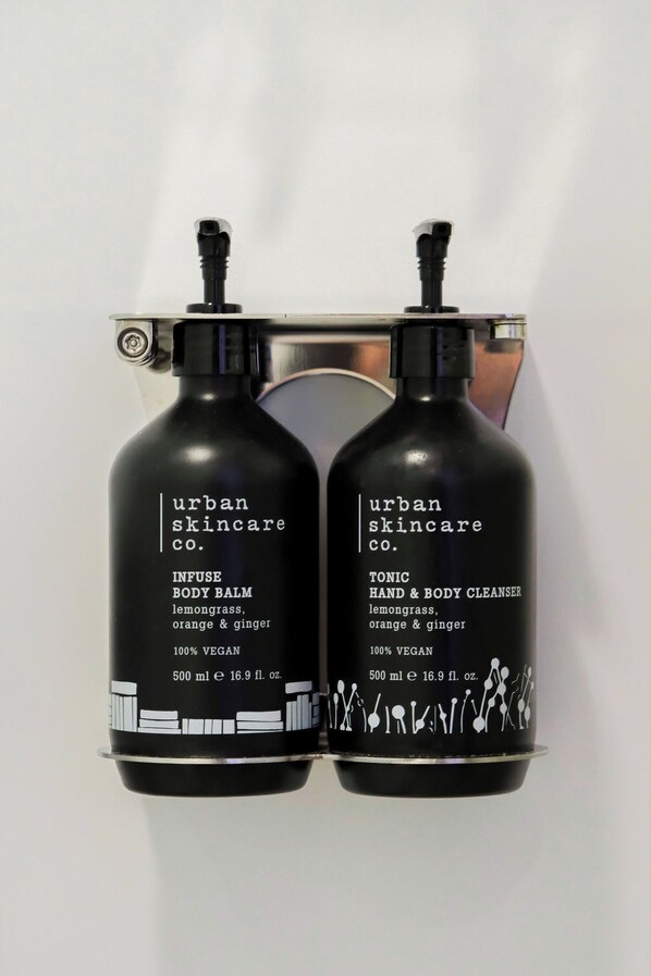 Dos botellas negras de productos Urban Skincare, una etiquetada como 'Infuse Body Balm' y la otra como 'Tonic Hand & Body Cleanser', ambas de 500 ml.