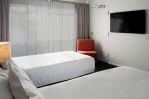 Een hotelkamer met een bed, een stoel, een televisie aan de muur en een raam met gordijnen.