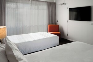 Habitación de hotel con una cama, una silla, un televisor en la pared y una ventana con cortinas.