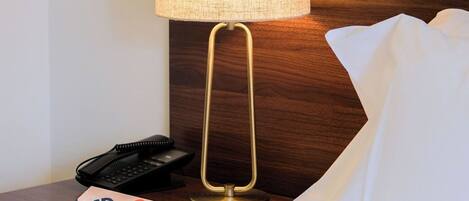 Habitación de hotel con una cama, una mesita de noche con lámpara, un teléfono y una tarjeta.