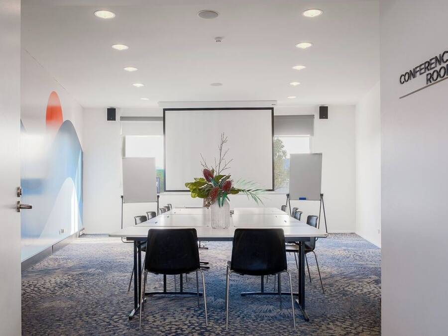 A conference room with a white table, black chairs, a projector screen, and a 'CONFERENCE ROOM' sign on the wall.