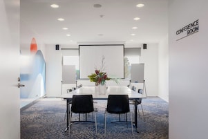A conference room with a white table, black chairs, a projector screen, and a 'CONFERENCE ROOM' sign on the wall.