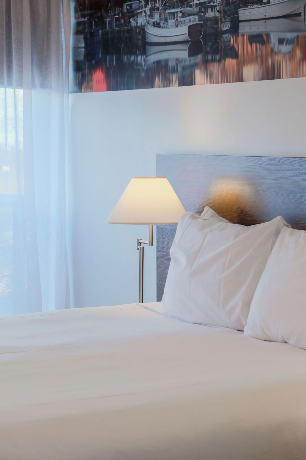 Una habitación de hotel con cama, lámpara y un cuadro en la pared.