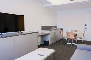 Een compacte hotelkamer met kitchenette, flatscreen televisie, een eethoek met stoelen en een bank.