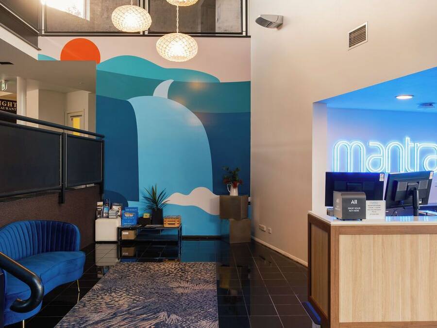 A hotel reception area with a blue wall mural, a reception desk, a blue chair, and a staircase.