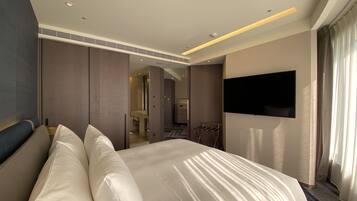 A modern hotel room with a large bed, a flat-screen TV mounted on the wall, and a bathroom visible through an open door.