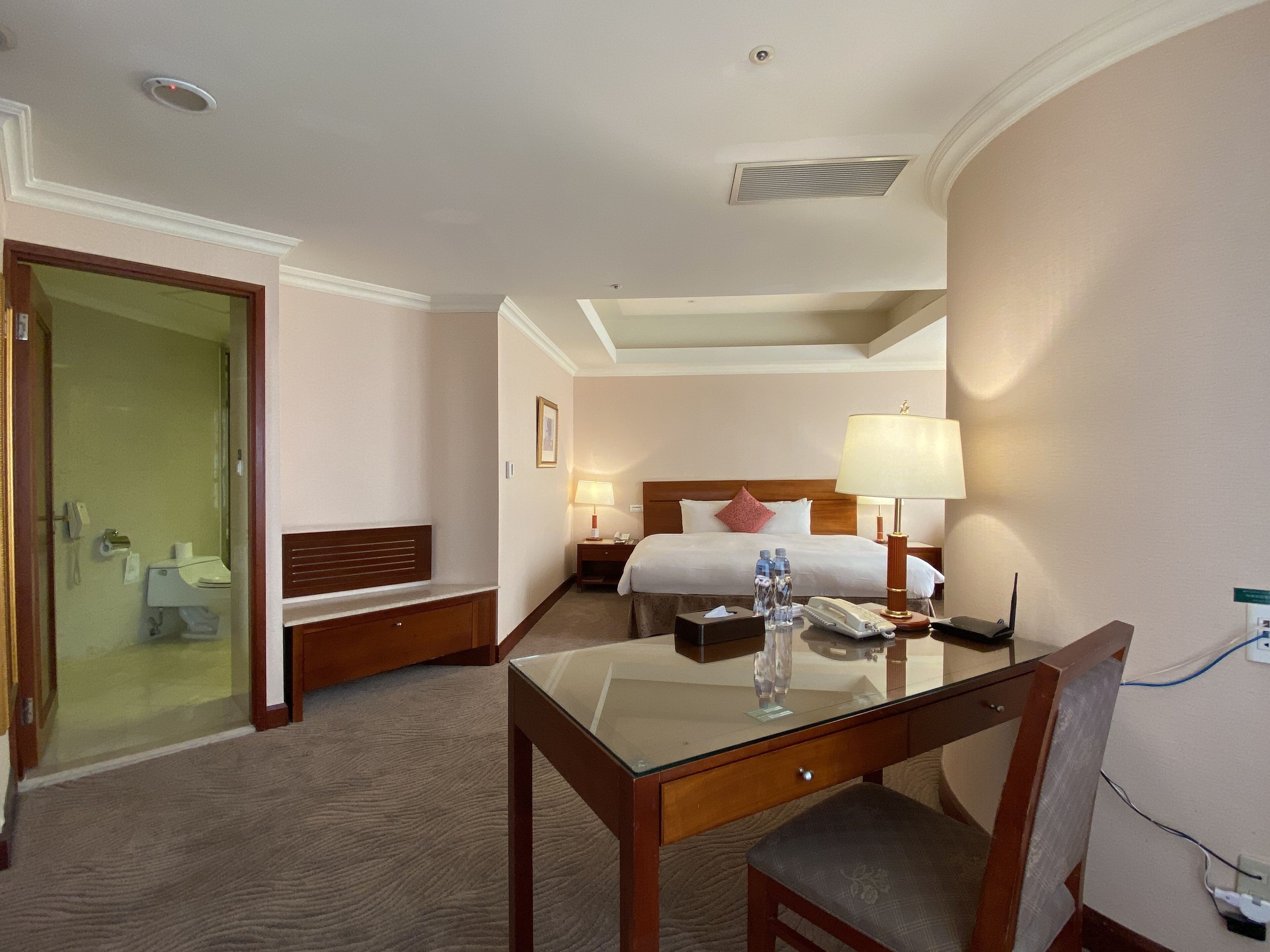 A hotel room with a bed, bedside tables, a desk, and a chair.
