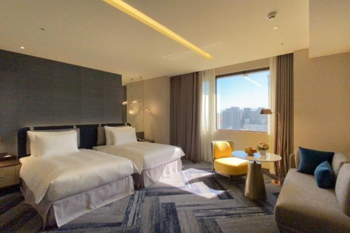 Habitación de hotel con dos camas, una mesita, una silla y un sofá.