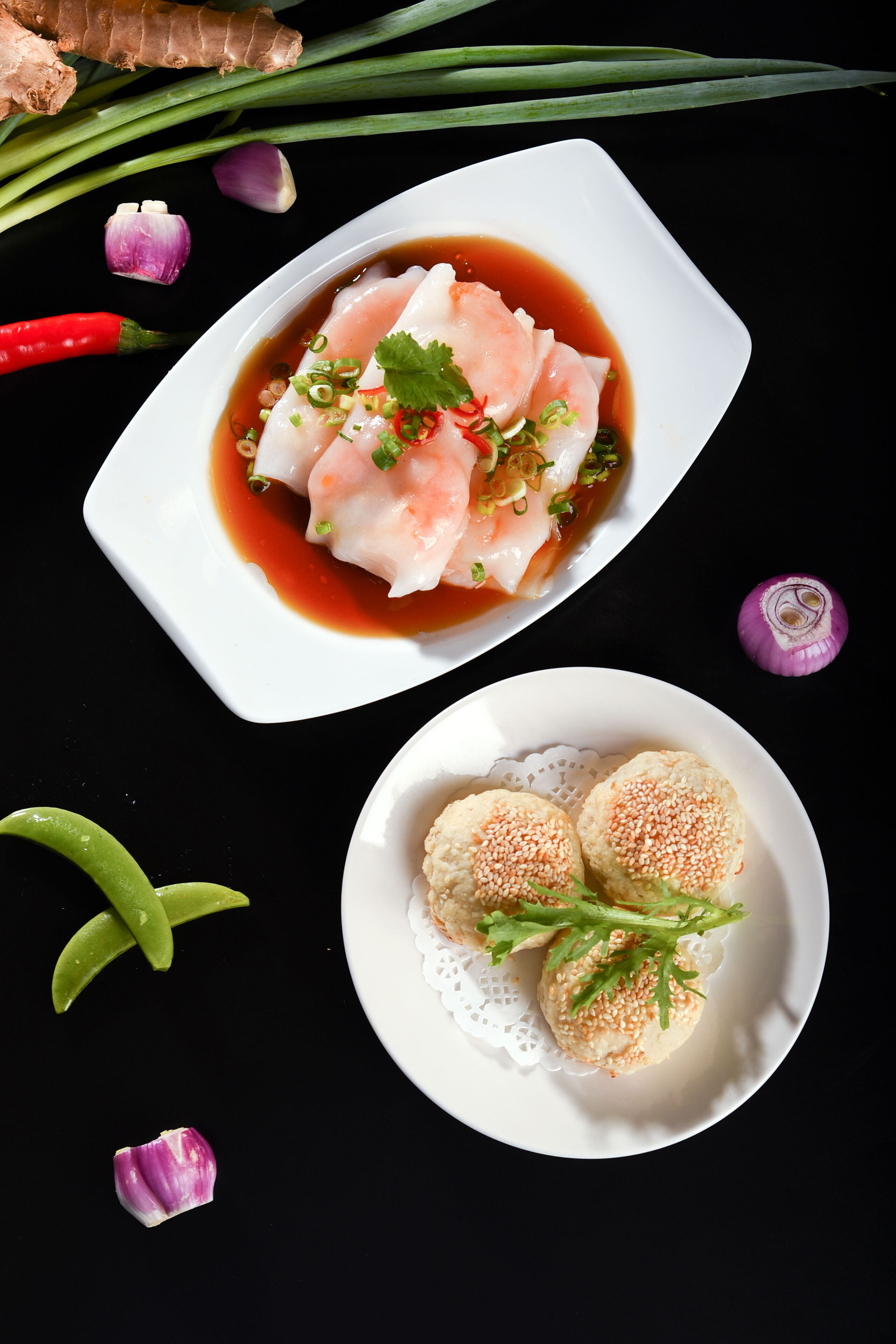 A plate of dumplings with a dipping sauce and garnishes, accompanied by a ginger root and green onions.