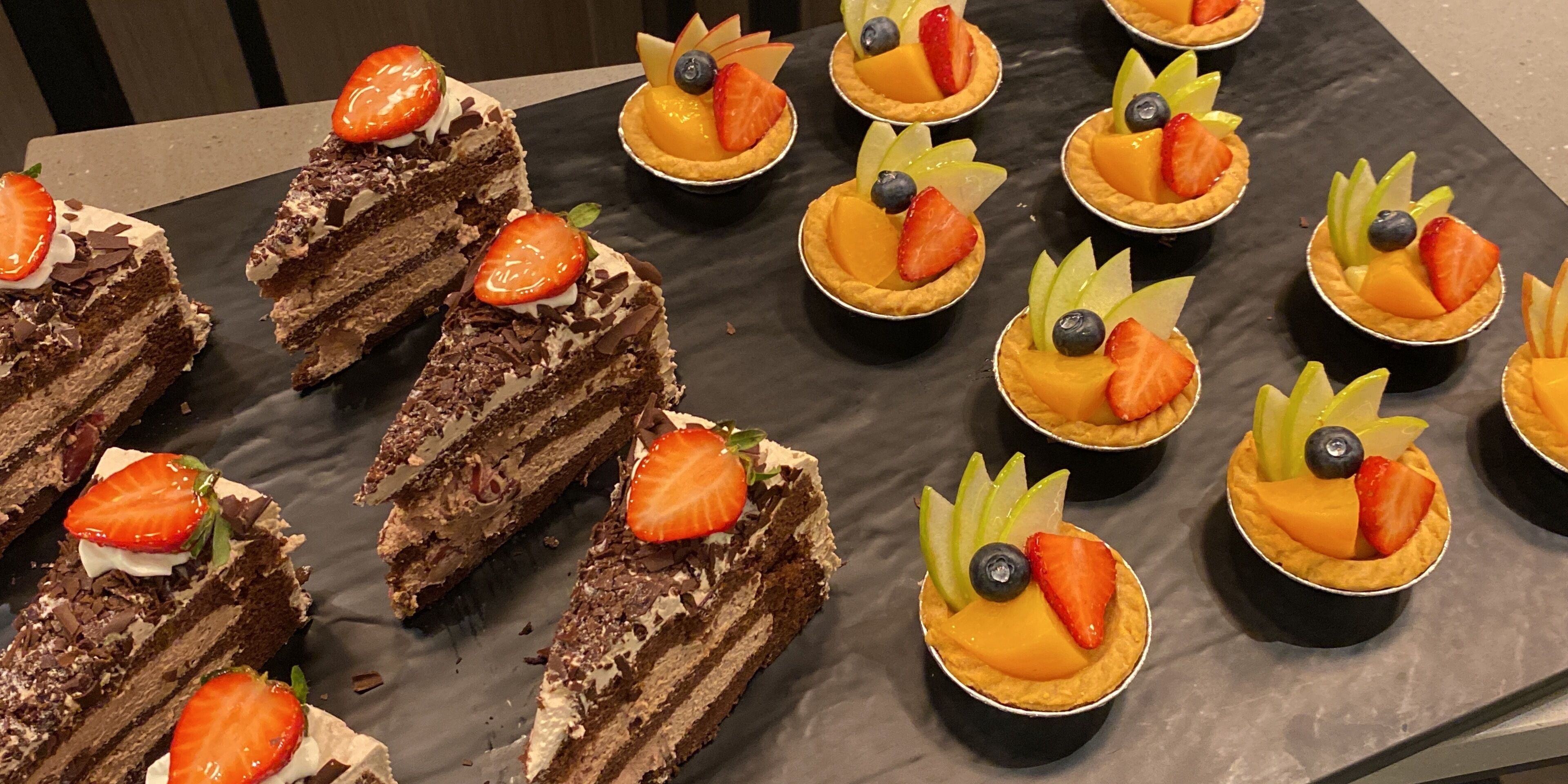 A variety of desserts arranged on a table, including chocolate cake slices and fruit-topped tarts.